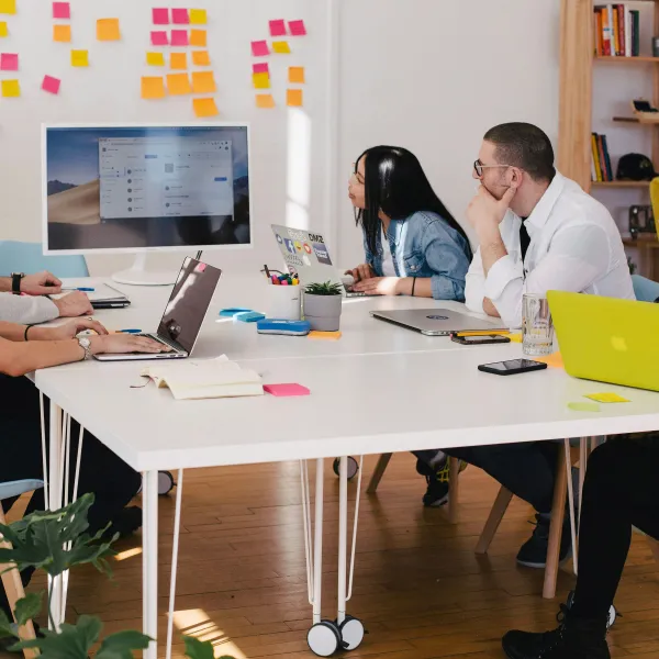 a group of people sitting around a table with laptops