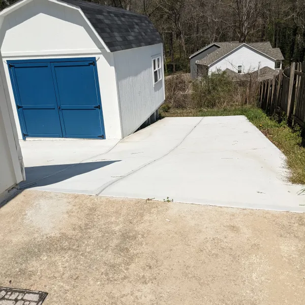 Clear view of a white garage with blue doors and a concrete driveway, surrounded by greenery and trees.