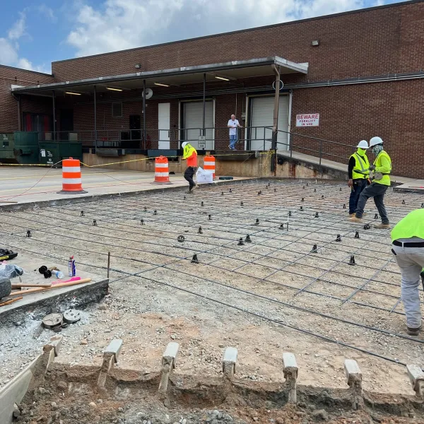 Workers laying rebar for concrete installation in a construction site with safety gear and equipment in view.
