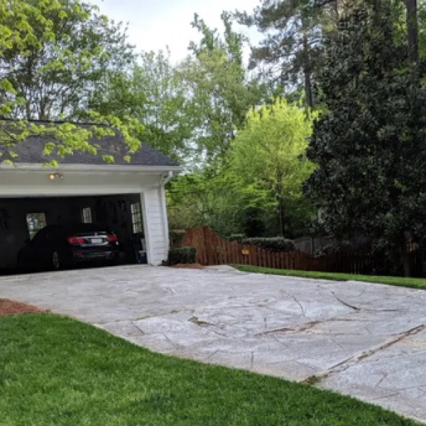 Concrete driveway leading to a two-car garage with a black car inside, surrounded by green trees and grass.