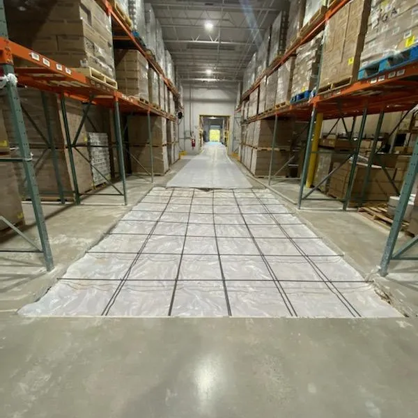 Wide aisle in a warehouse lined with storage racks and a plastic sheet on the floor.