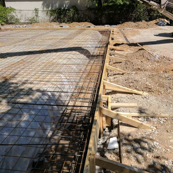 Concrete slab foundation with steel reinforcement grid and wooden formwork under construction on a sunny day.