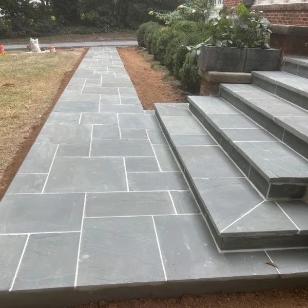 Newly installed gray stone tile walkway and stairs leading to a brick house with surrounding garden.