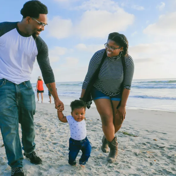 a man and woman holding hands with a child on a beach