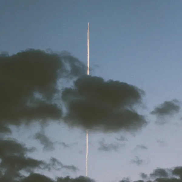Vertical contrail of an airplane piercing through dark clouds in a blue sky at dusk.