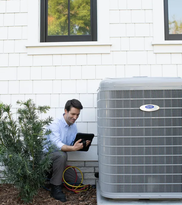 Technician inspects residential air conditioning unit beside house using a tablet with connected gauges.