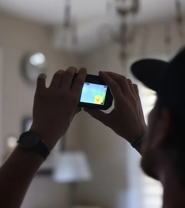 Person using a thermal imaging camera indoors to detect heat patterns on a wall.