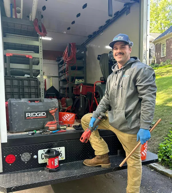 A smiling technician in work attire stands by a service truck filled with tools and equipment for plumbing.