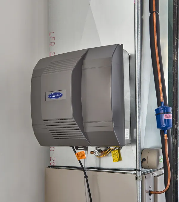 Close-up of a Carrier HVAC system with accompanying pipes and electrical wiring installed in a utility room corner.