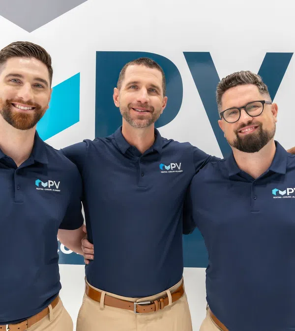 Three smiling men in navy polo shirts with PV logo standing in front of branded wall, arms around each other.