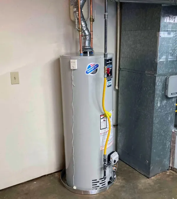 Tall gray water heater with pipes, yellow gas line, and ventilation duct in a basement utility area.