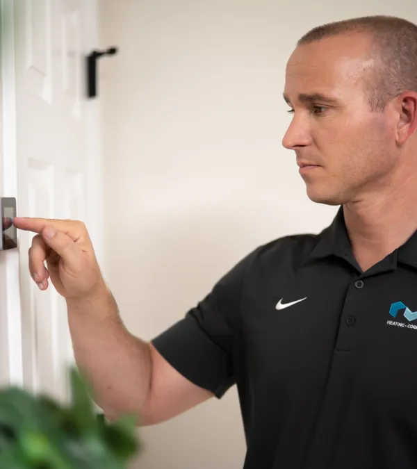 Technician in black PV Heating shirt adjusting a thermostat on a white wall in a residential setting