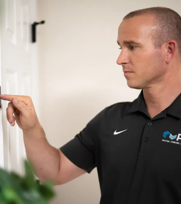 Technician in black PV Heating shirt adjusting a thermostat on a white wall in a residential setting
