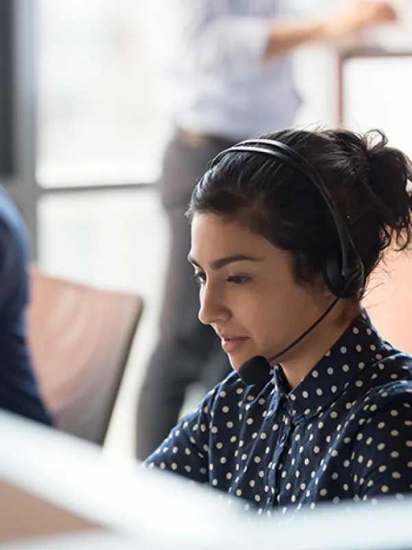 Smiling customer service representative with curly hair wearing a headset in a modern office environment.