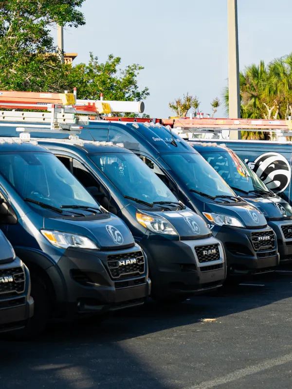 Row of black RAM vans with ladders parked in a lot under clear sky and palm trees.