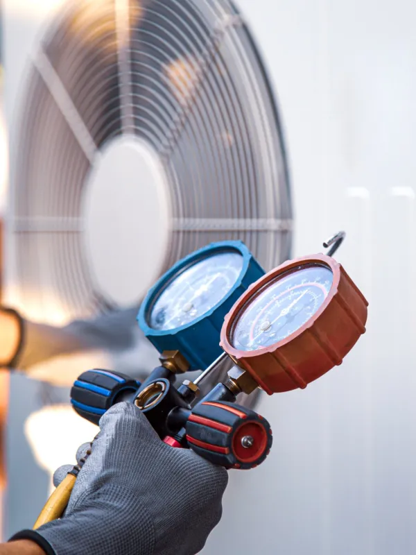 Technician adjusting HVAC pressure gauges while servicing an air conditioning unit outdoors with gloves.