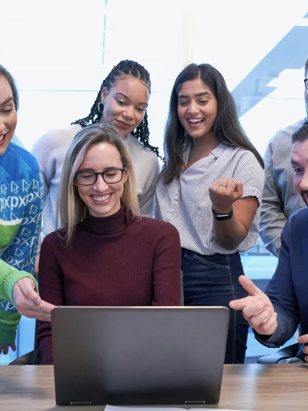 Diverse group of colleagues excitedly looking at a laptop screen together in a modern office.