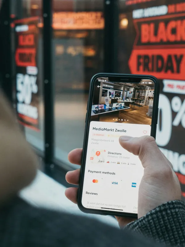 Person holding smartphone displaying MediaMarkt Zwolle app with Black Friday sale signs in background