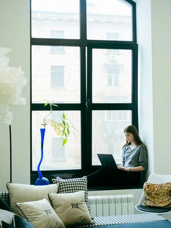 a woman sitting on a couch with a laptop in front of a window