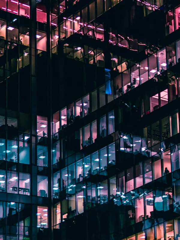 Night view of a modern office building with colorful illuminated windows and reflections on glass facade.