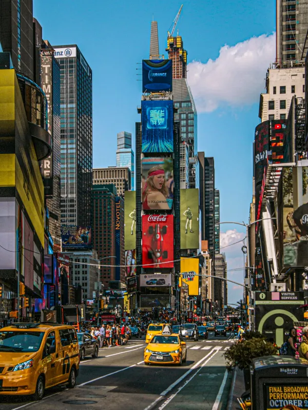 Busy New York City street with yellow taxis, skyscrapers, and vibrant digital billboards on a clear day