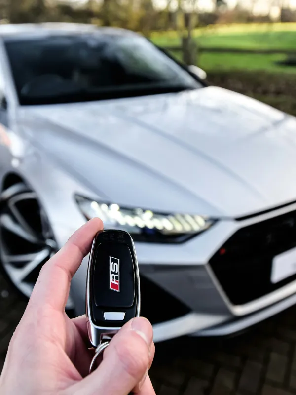 a hand holding a cell phone in front of a car