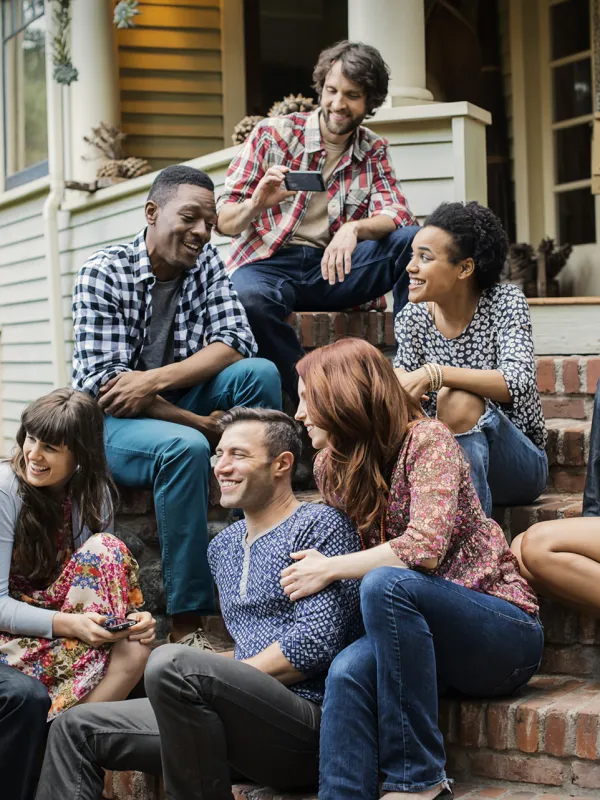 Group of young adults socializing and laughing together on a house porch steps on a sunny day