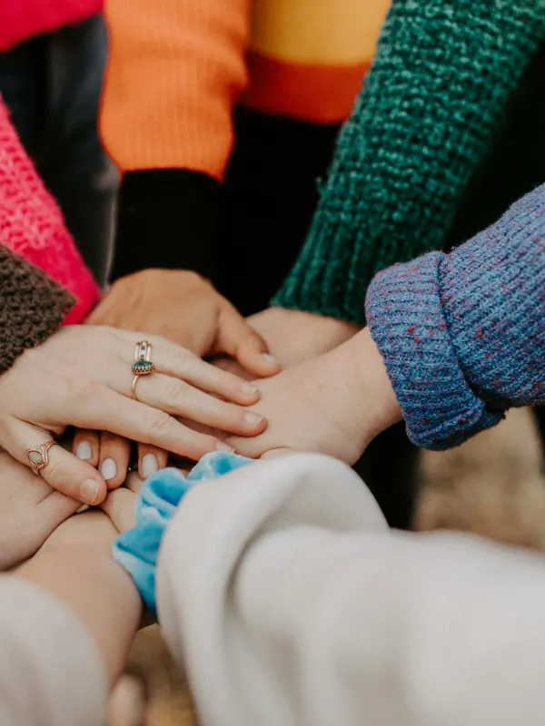 Group of people putting hands together in a show of unity and teamwork with colorful sweaters.