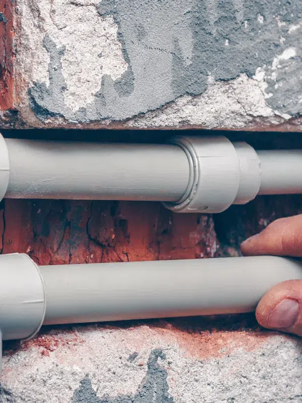 Hands installing gray PVC pipes on a brick wall during plumbing work or construction project.