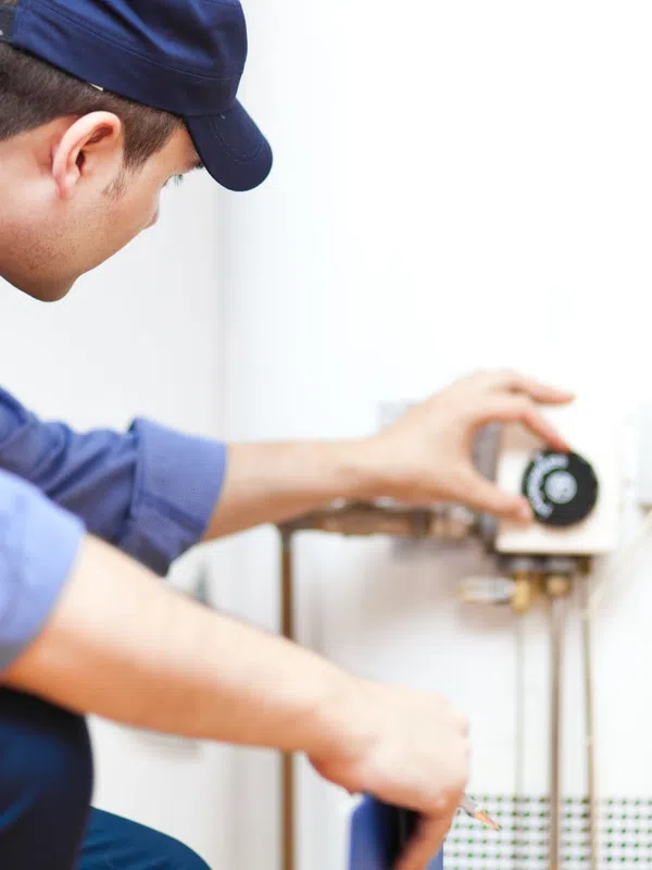 Technician adjusting temperature control on a white water heater in a maintenance setting indoors.