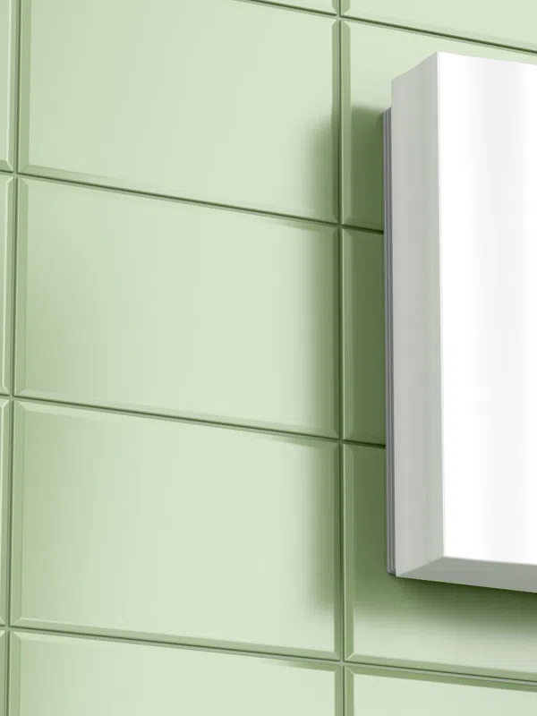 White electric water heater mounted on green tiled wall with control knobs on the front panel