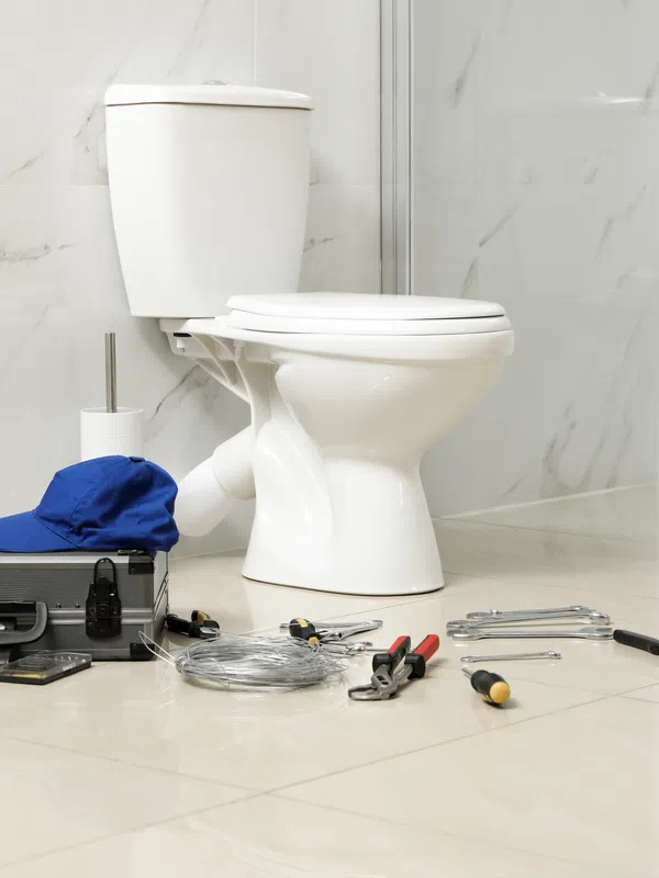 Plumber's tools, blue cap, and toolbox arranged on bathroom floor near white toilet and patterned wall.