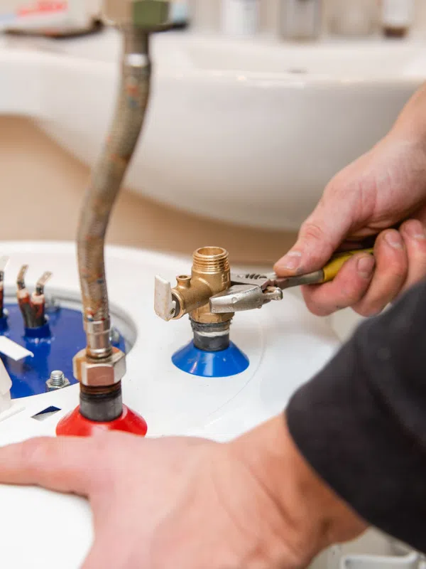 Technician repairing a water heater using a wrench on water inlet and outlet connections under a sink