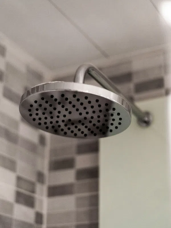 Close-up of a modern round showerhead mounted on a wall with grey and white tiled background