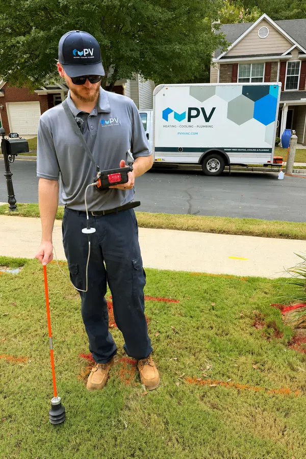 Technician wearing PV HVAC uniform using equipment to measure gas or pressure outside a residential home.