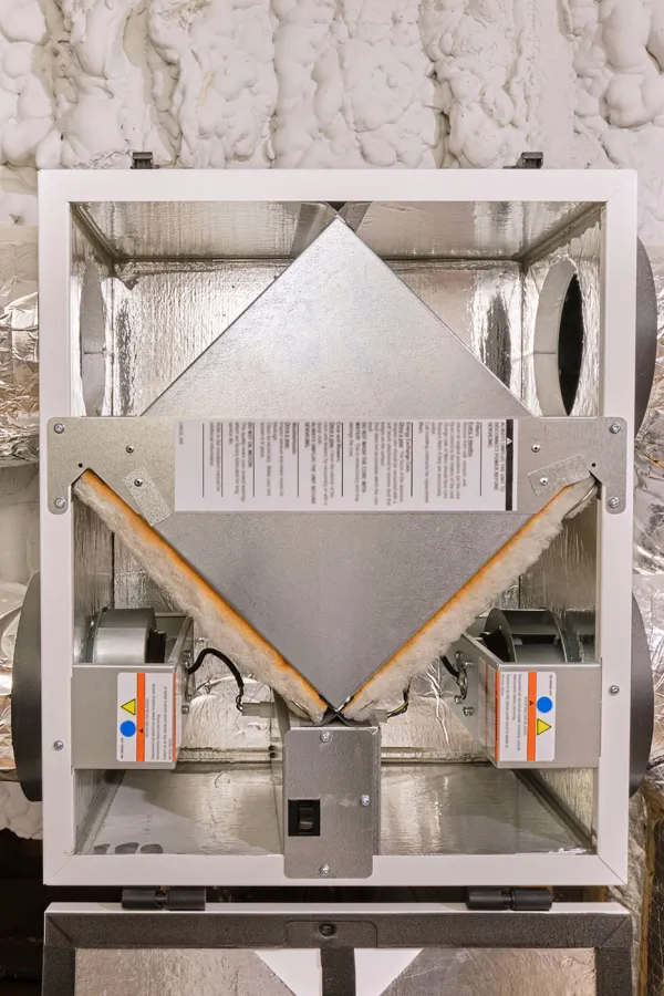 Ceiling-mounted heat recovery ventilator with insulated ductwork and spray foam insulation in attic space