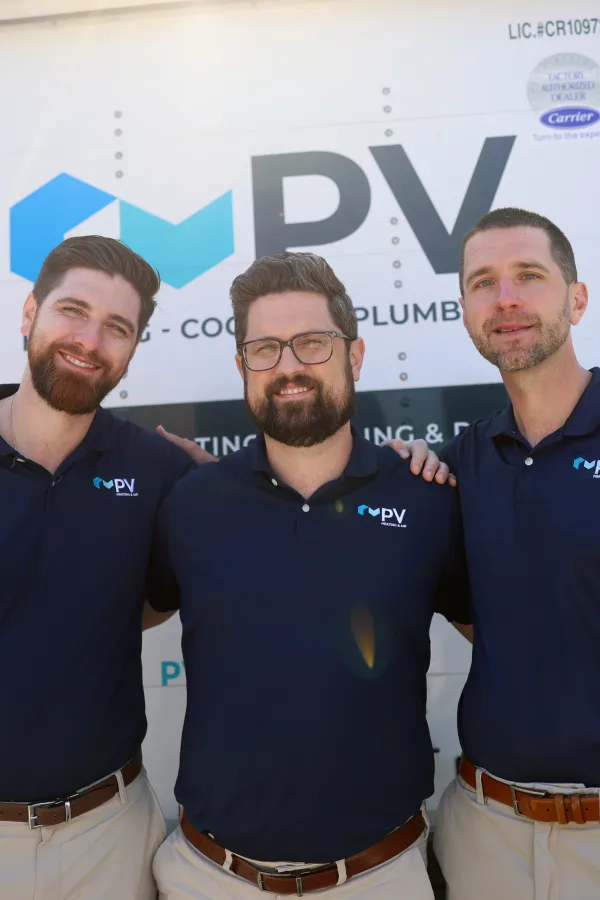 Three men wearing matching navy blue polo shirts with PV Heating Cooling Plumbing logo stand in front of a service truck.