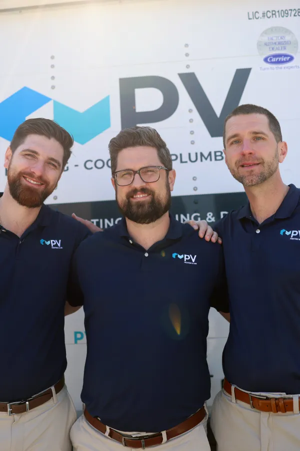 Three men wearing matching navy blue polo shirts with PV Heating Cooling Plumbing logo stand in front of a service truck.