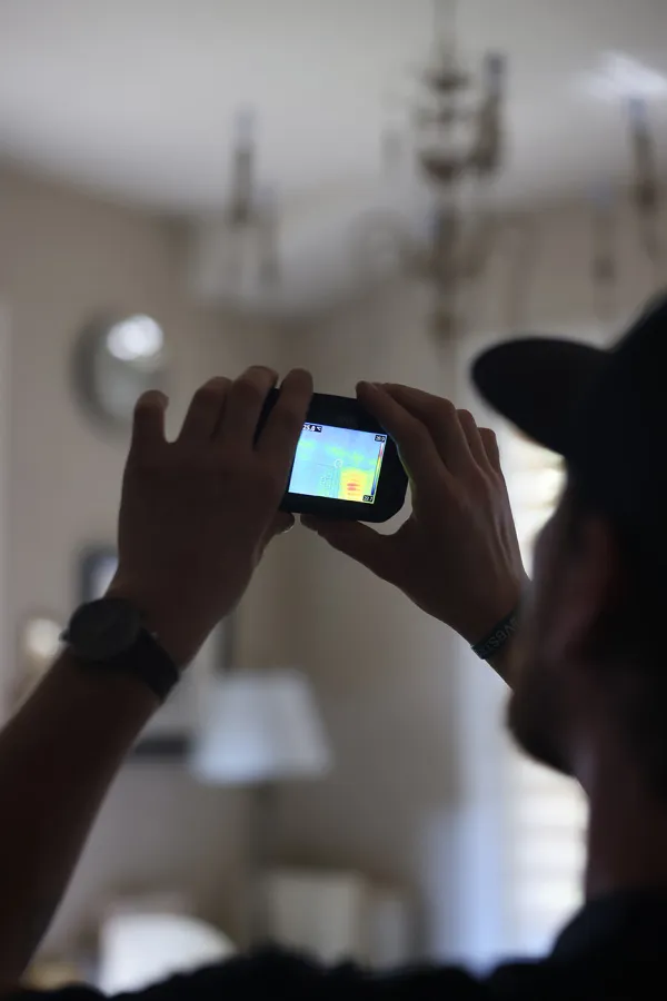 Person using a thermal imaging camera indoors to detect heat patterns on a wall.