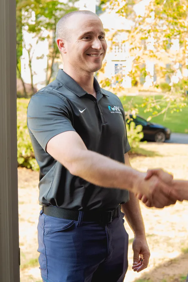 Professional technician greeting homeowner with a handshake at the front door in a suburban neighborhood.