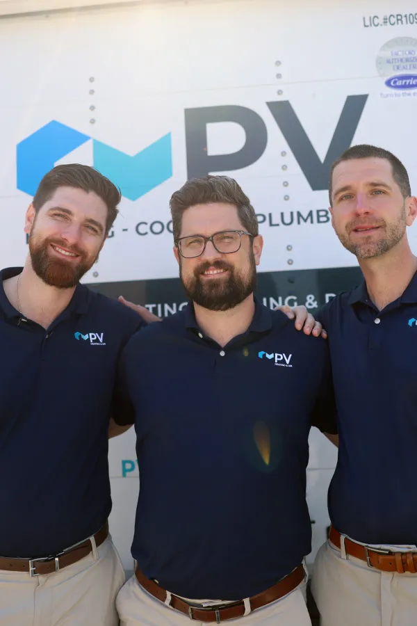 Three smiling men wearing matching PV company navy shirts standing in front of a service truck outdoors