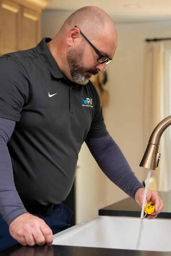 Technician testing water flow from kitchen faucet using a yellow tool in a modern kitchen sink area.