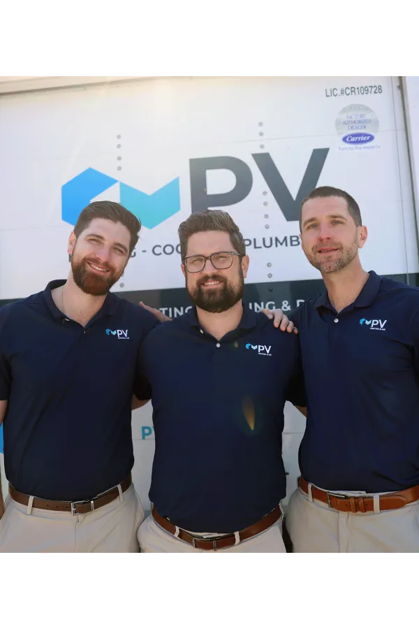 Three men in matching navy shirts and khaki pants smiling in front of a PV heating and cooling plumbing truck