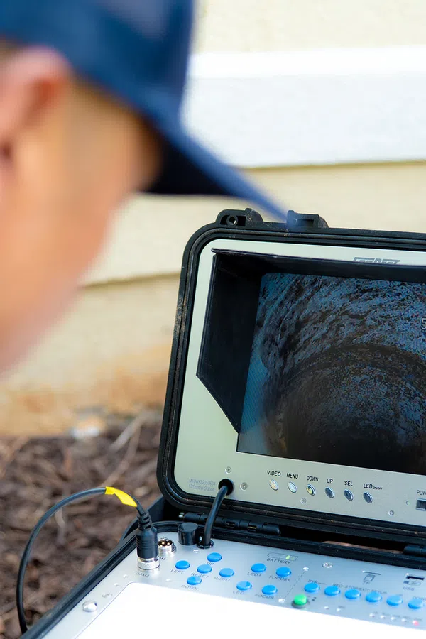 Technician inspecting a pipe interior using a portable video inspection camera monitor outdoors near a building.