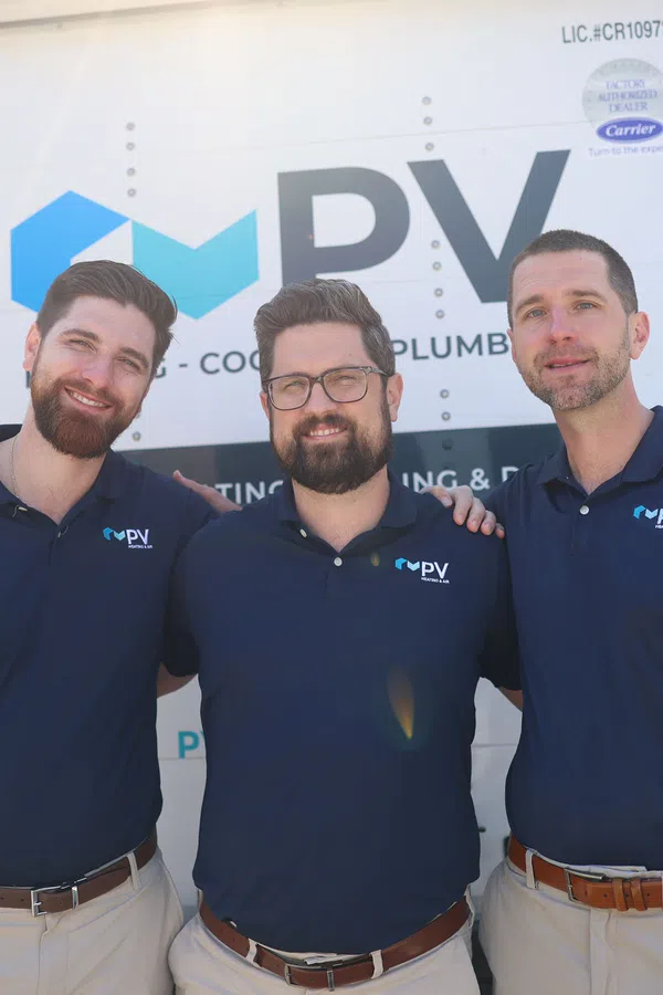 Three men in branded navy blue shirts standing and smiling in front of a company truck with PV logo.