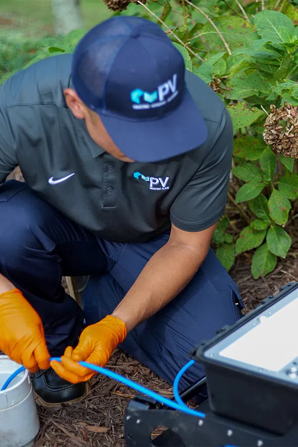 Technician in blue uniform and orange gloves working with fiber optic cables near a house garden.