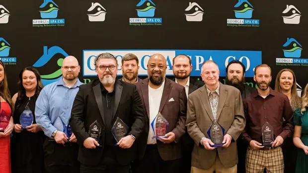 Group of 21 diverse people holding awards standing in front of backdrop with business logos at formal event.