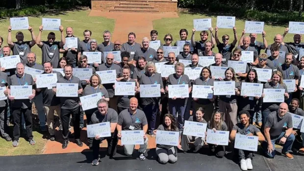 Large group of people outdoors holding certificates, posing for a group photo on a sunny day.