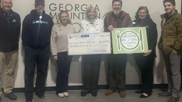 Group of seven people holding donation checks in front of Georgia Mountain Food Bank sign.