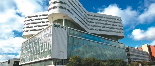 Modern multi-story hospital building with glass facade and curved upper floors under blue sky with clouds.